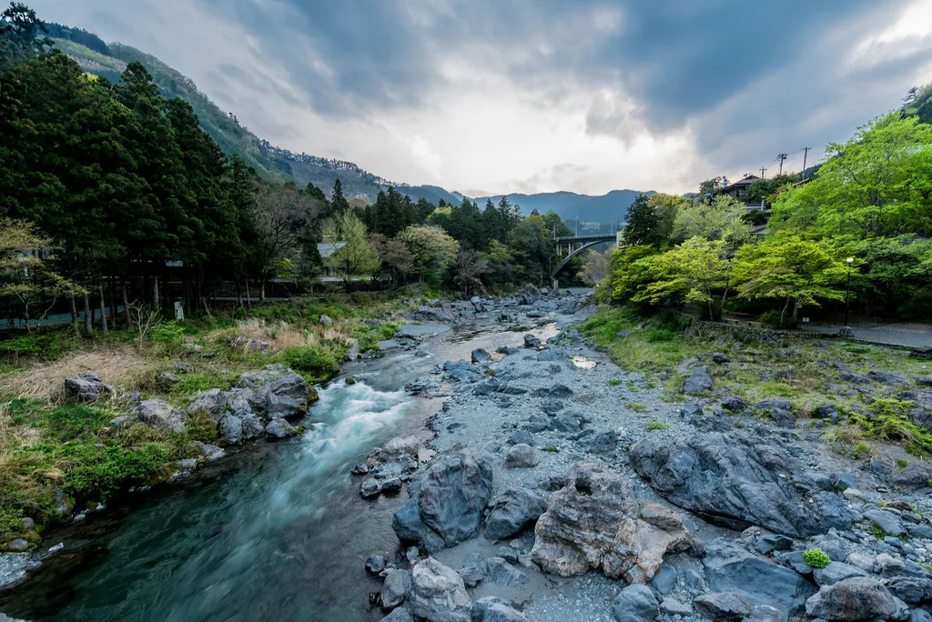 A rocky river running between green, wooded hills