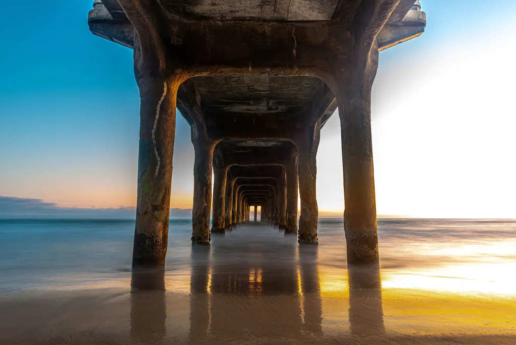 Looking down the underside of a pier toward a gold sunset