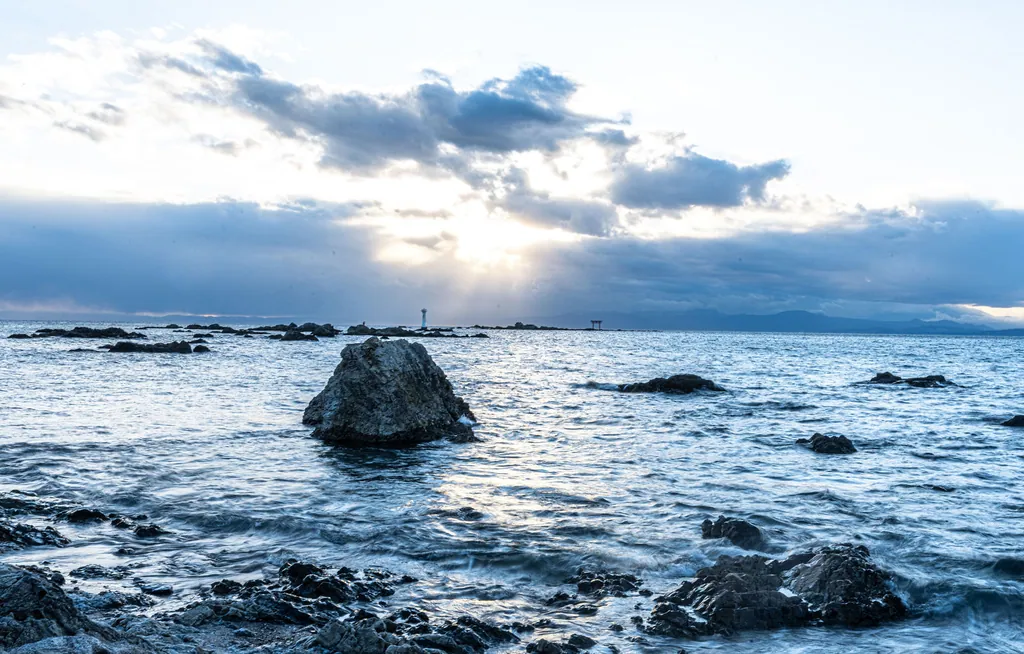 A lone rock in a rough sea under a bright, cloudy sky